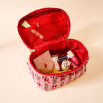 Open red cosmetic bag with floral base containing various items on a beige background