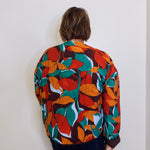 Person wearing a colorful leaf-patterned jacket against a plain background