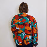 Person wearing a colorful leaf-patterned jacket against a plain background