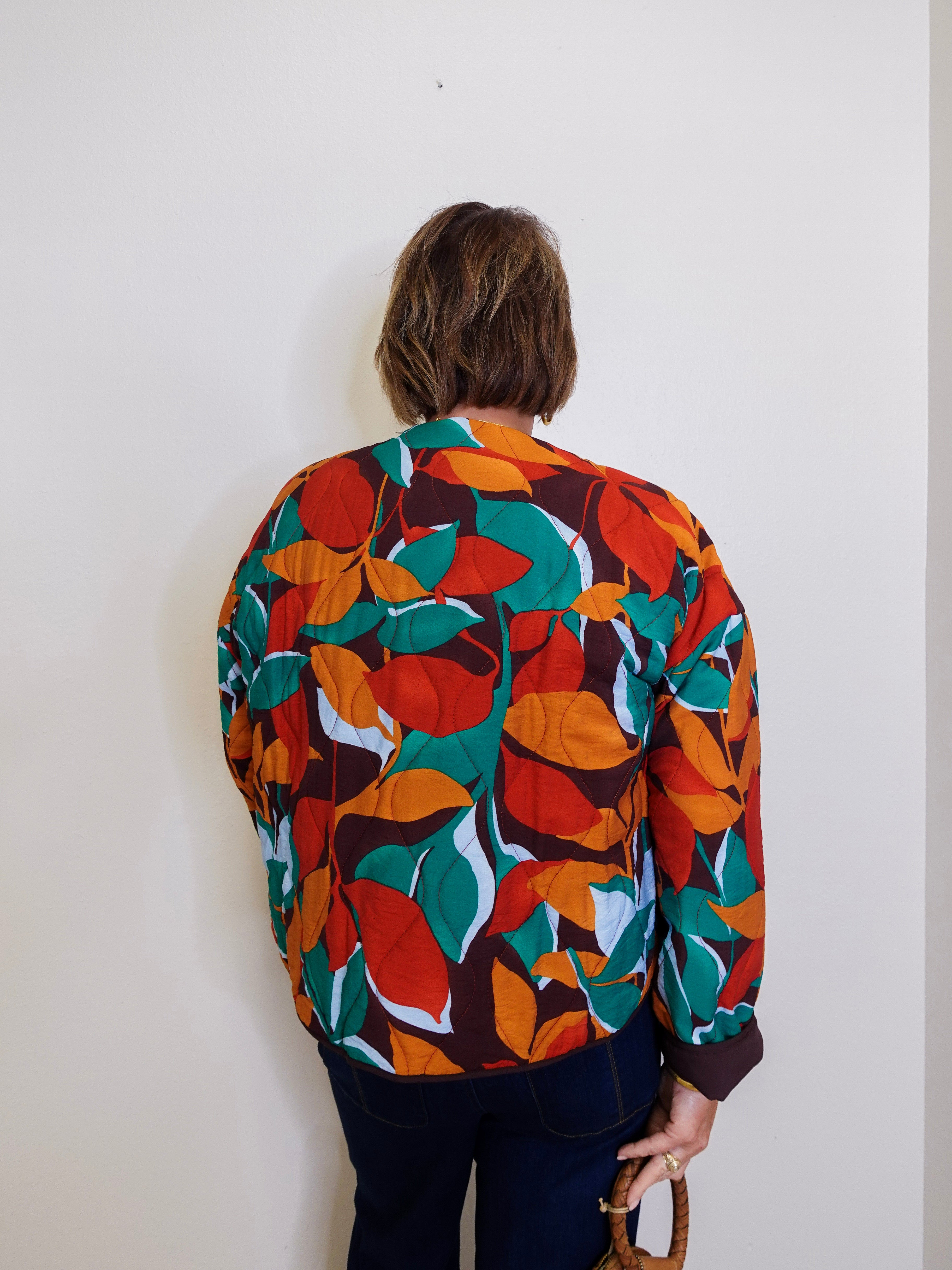 Person wearing a colorful leaf-patterned jacket against a plain background