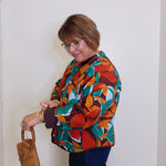 Woman wearing a colorful patterned shirt holding a brown bag against a white background