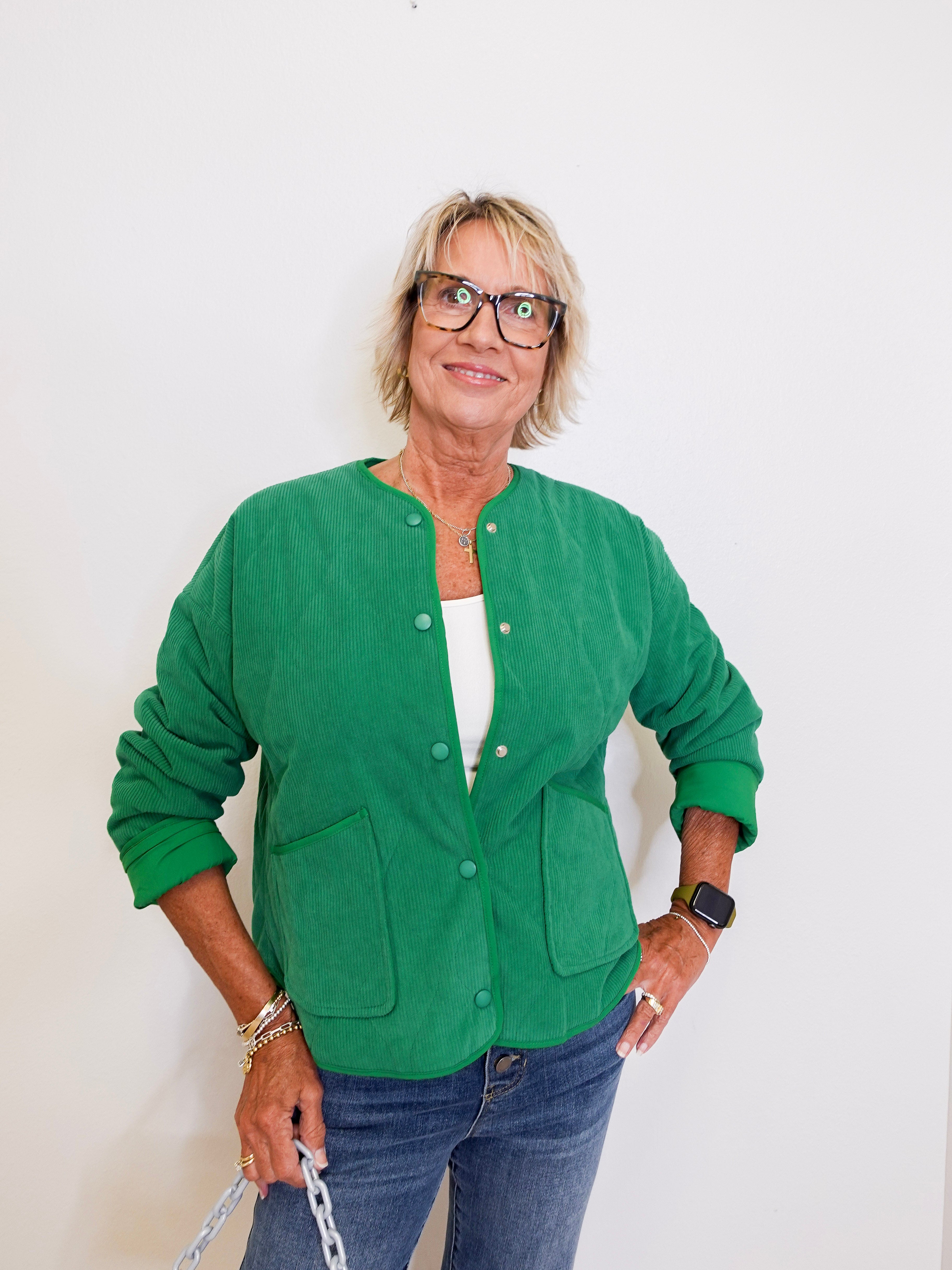 Woman wearing a green jacket and glasses against a white background