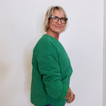 Person wearing a green sweater and blue jeans against a white background