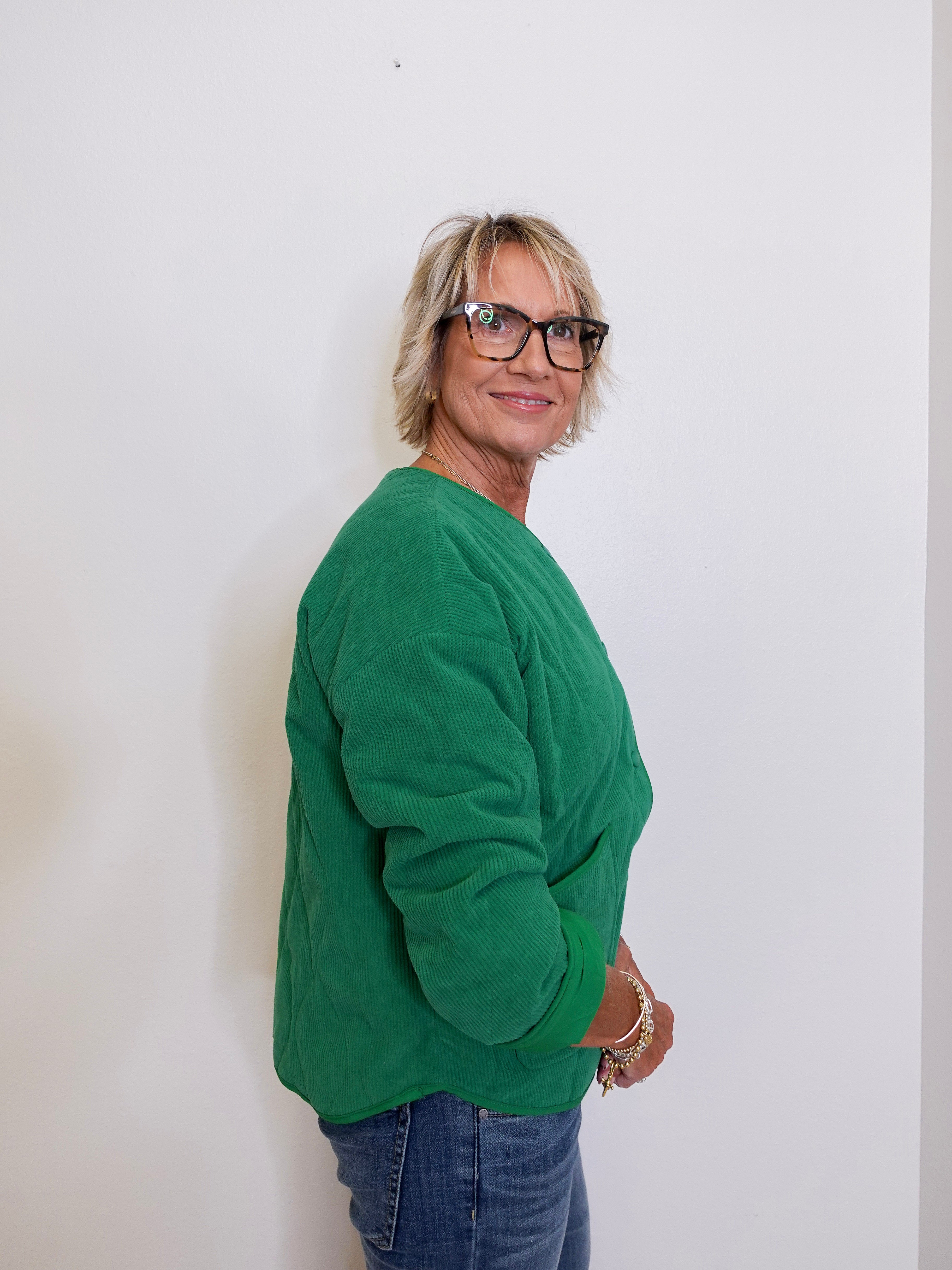 Person wearing a green sweater and blue jeans against a white background