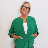 Woman wearing a green cardigan over a white top and blue jeans, standing against a plain background.