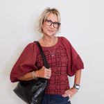 Woman wearing a red blouse with a geometric pattern, holding a black bag against a white background