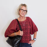Woman wearing a red blouse with a geometric pattern, holding a black bag against a white background