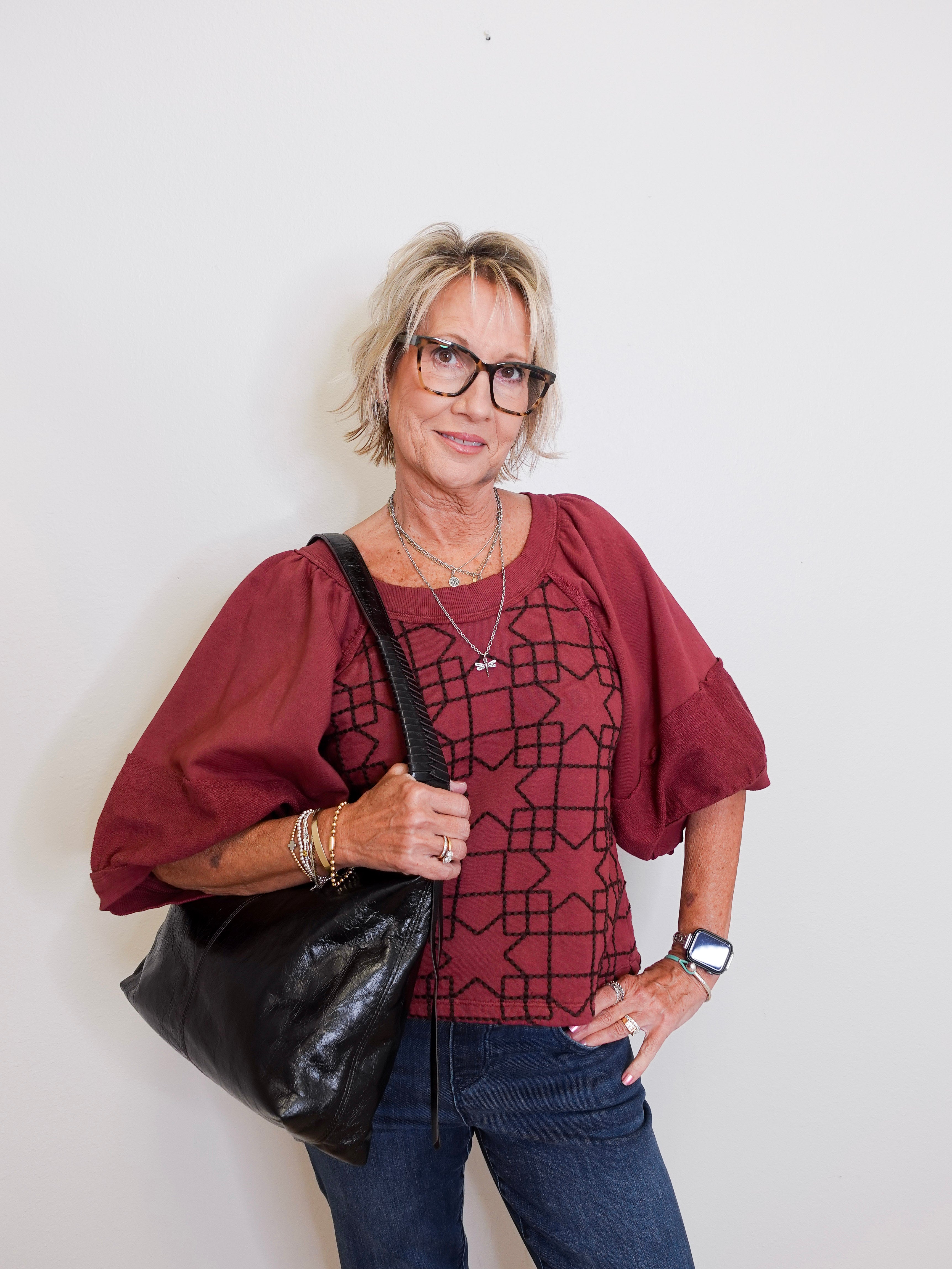 Woman wearing a red blouse with a geometric pattern, holding a black bag against a white background
