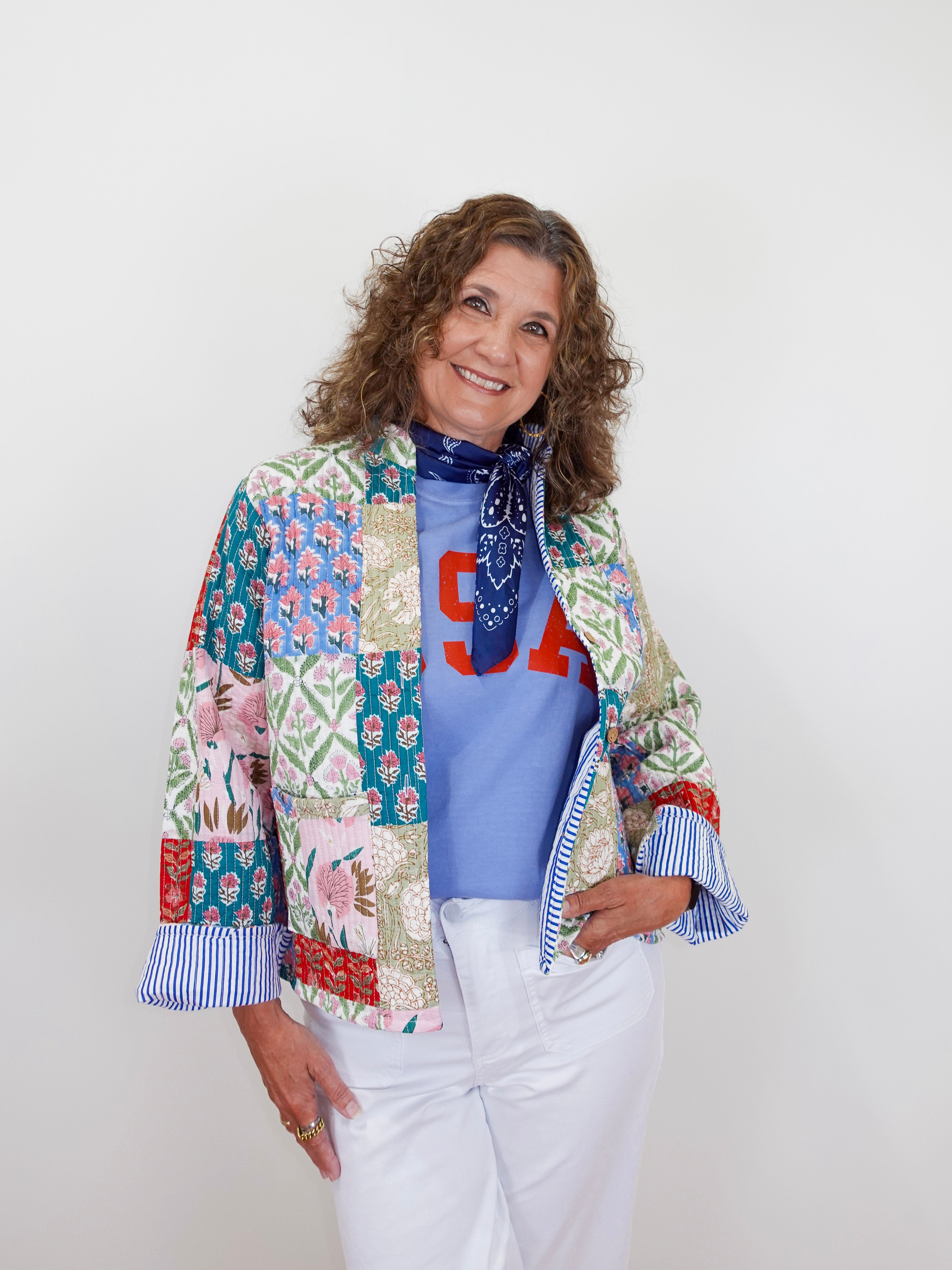 Woman wearing a colorful patchwork jacket over a blue shirt with red letters on a white background