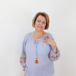 Woman wearing a light blue blouse with colorful sleeves against a white background