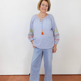 Woman wearing a light blue blouse with colorful sleeves and jeans against a white wall.