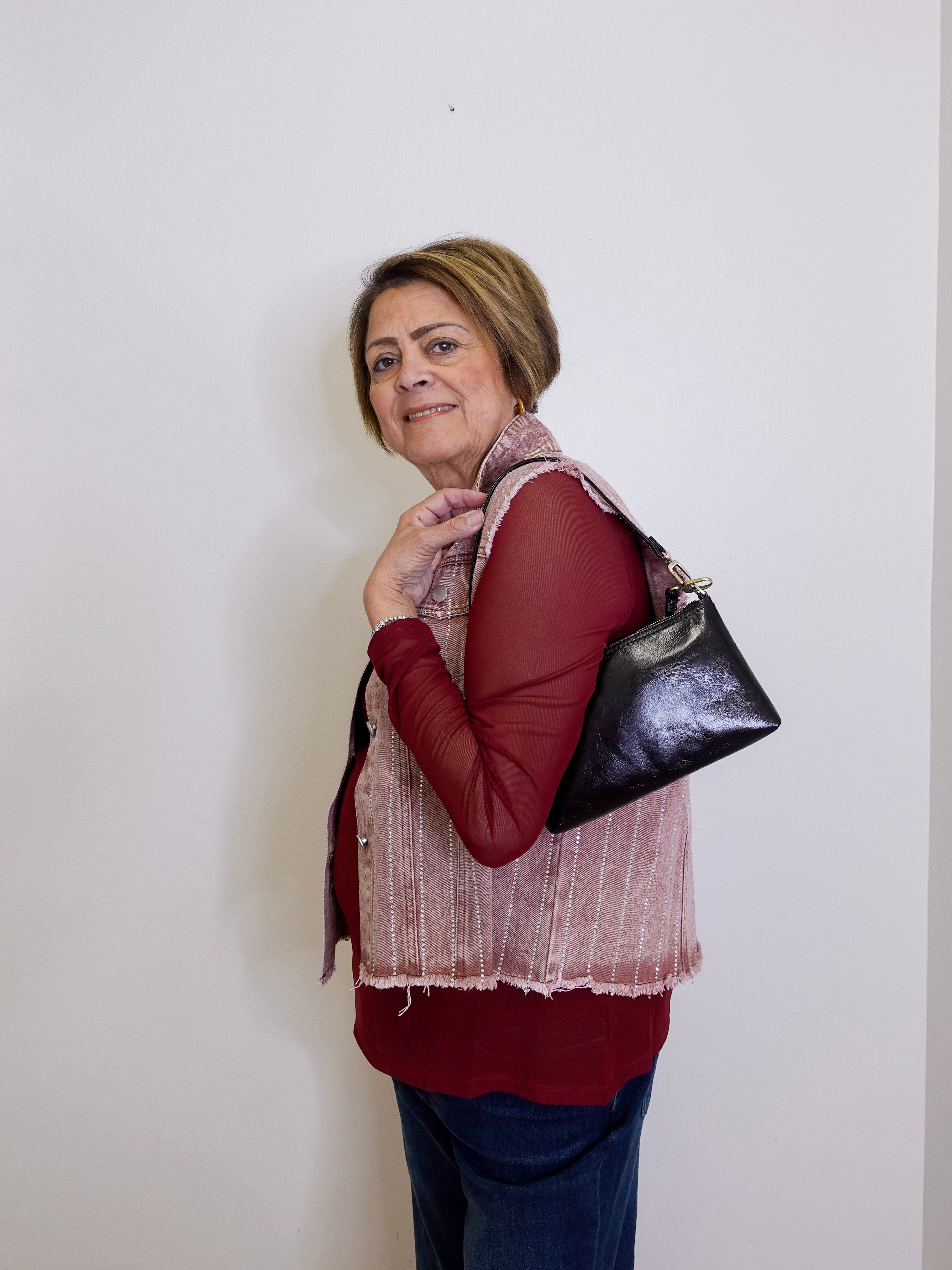 Woman wearing a red shirt and patterned vest, holding a black handbag against a white background
