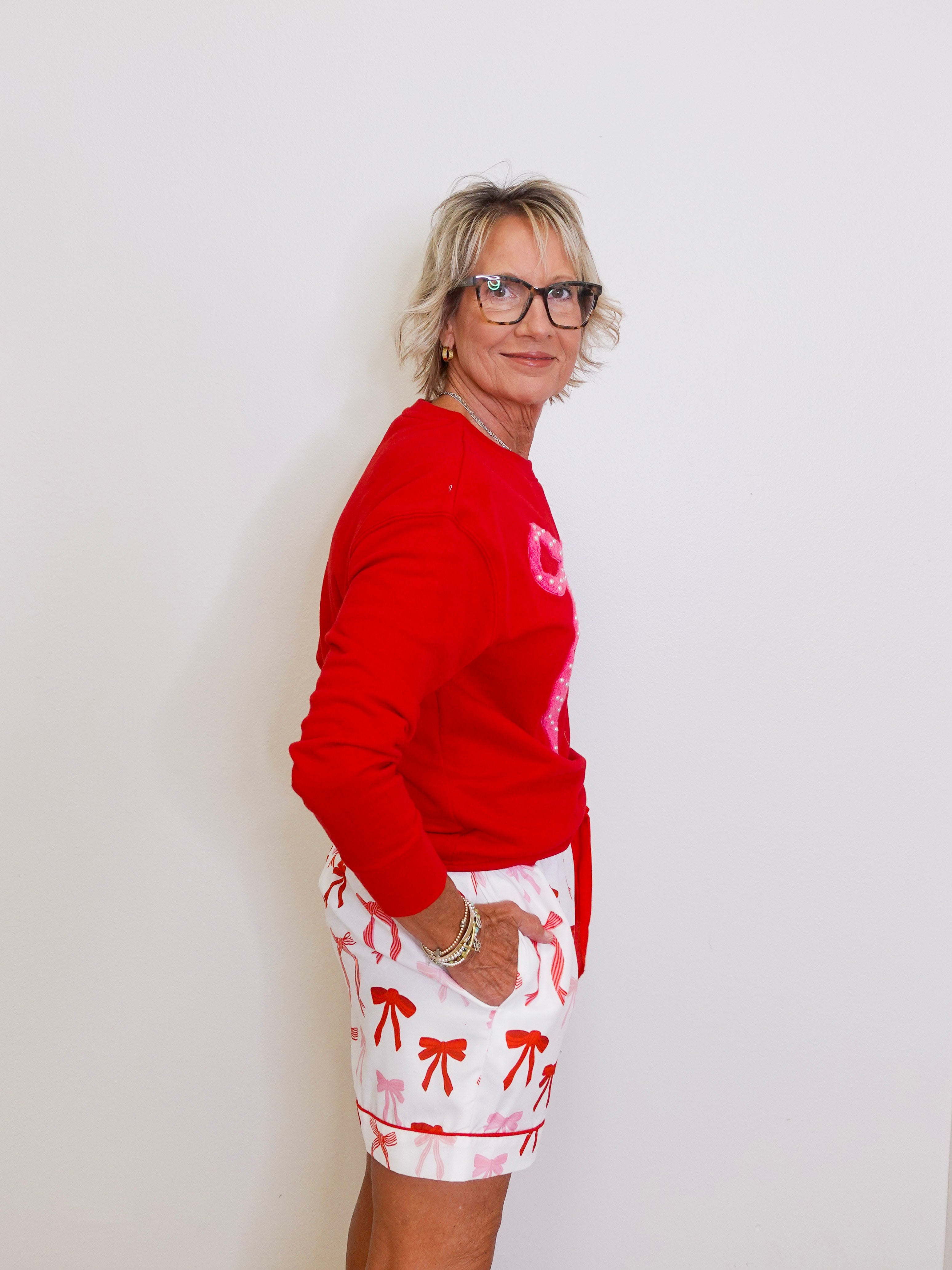 Person wearing a red sweater and white shorts with red patterns against a plain background