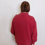 Person wearing a red sweater against a white wall
