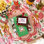 Decorative table setting with a Prosecco bottle, popcorn, and a Christmas-themed ornament on a floral tablecloth.