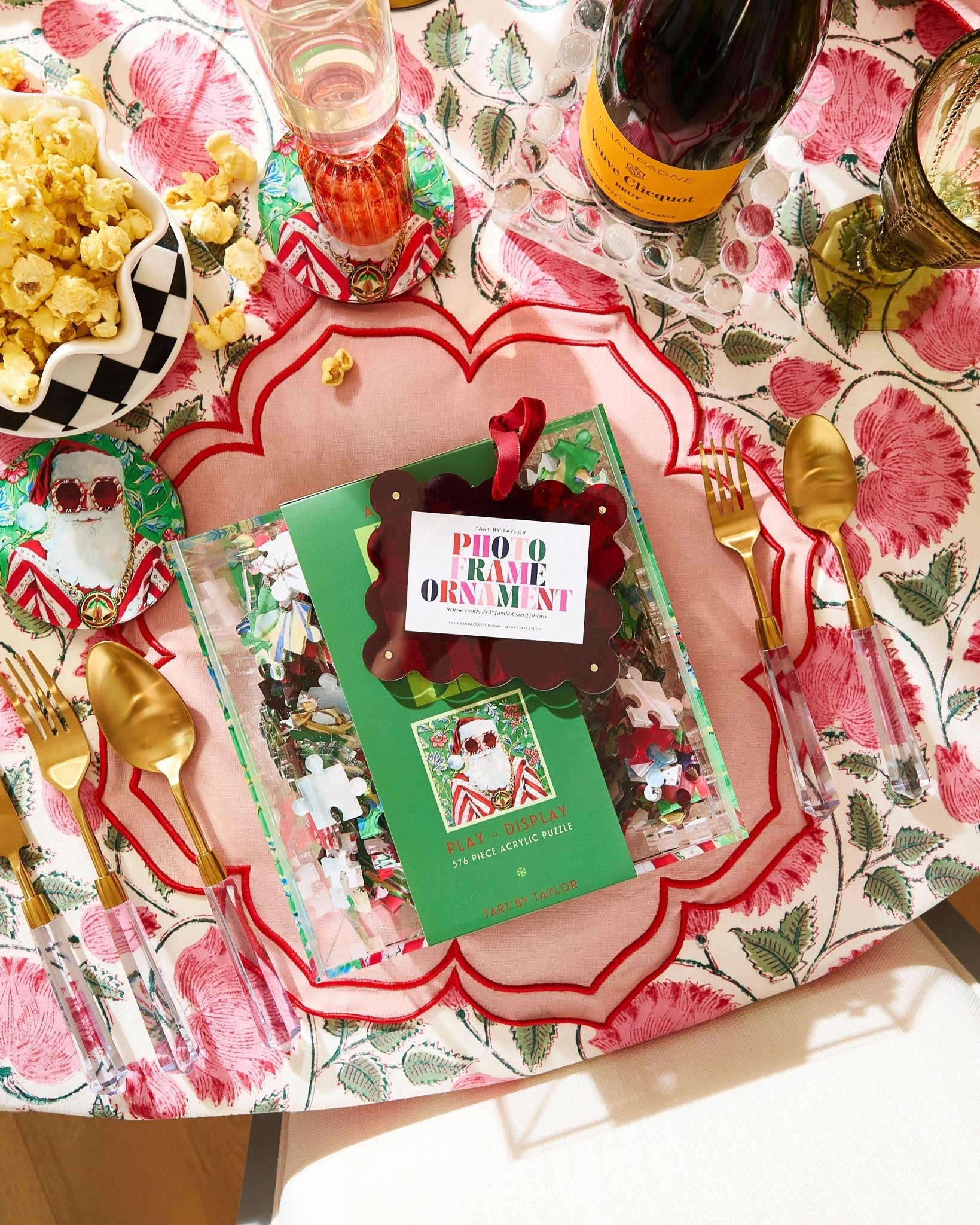 Decorative table setting with a Prosecco bottle, popcorn, and a Christmas-themed ornament on a floral tablecloth.