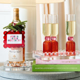 Wine bottle with decorative tag, glasses of champagne, and books on a table.