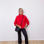Woman in a red sweater and black pants standing against a white wall.