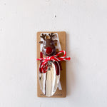 Metal bottle opener shaped like a reindeer on a cardboard backing with red string, against a white background.