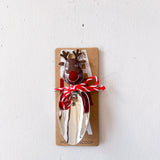 Metal bottle opener shaped like a reindeer on a cardboard backing with red string, against a white background.