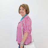 Woman wearing a red and white checkered shirt with a white bag against a white wall.