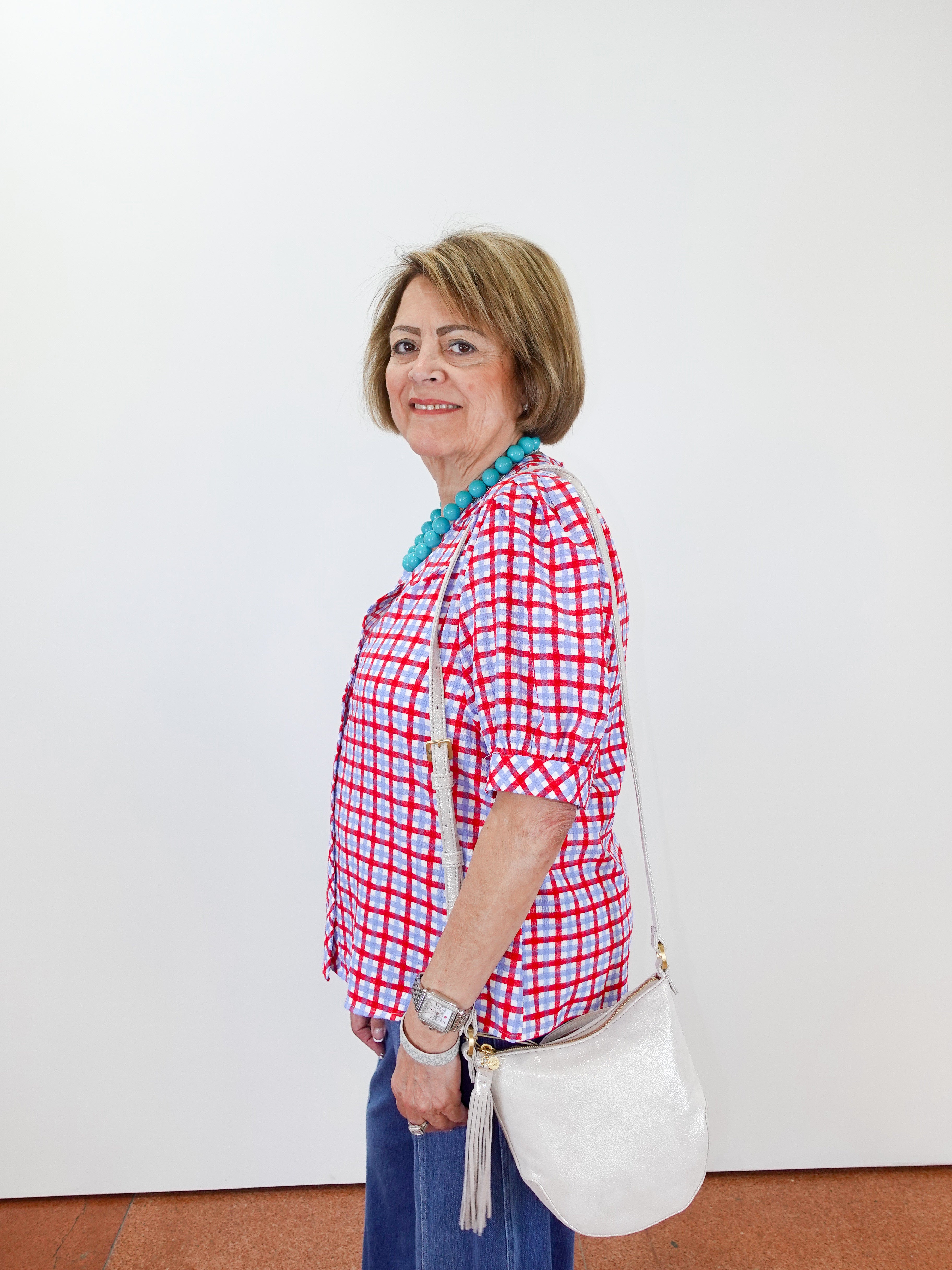 Woman wearing a red and white checkered shirt with a white bag against a white wall.