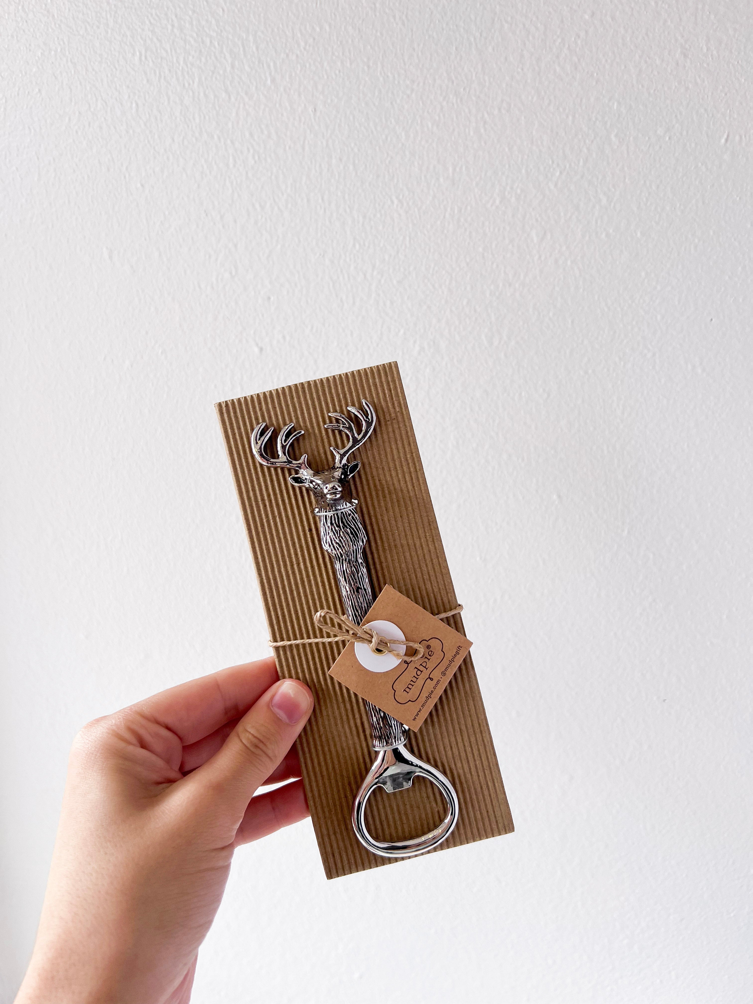Hand holding a deer-shaped bottle opener on a brown card with a white background