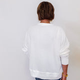 Person wearing a white sweatshirt and blue jeans against a plain background