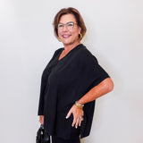 Woman wearing a black outfit with glasses against a white wall