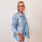 Person wearing a denim jacket and white pants against a plain background