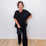 Woman wearing a black outfit standing against a white wall.