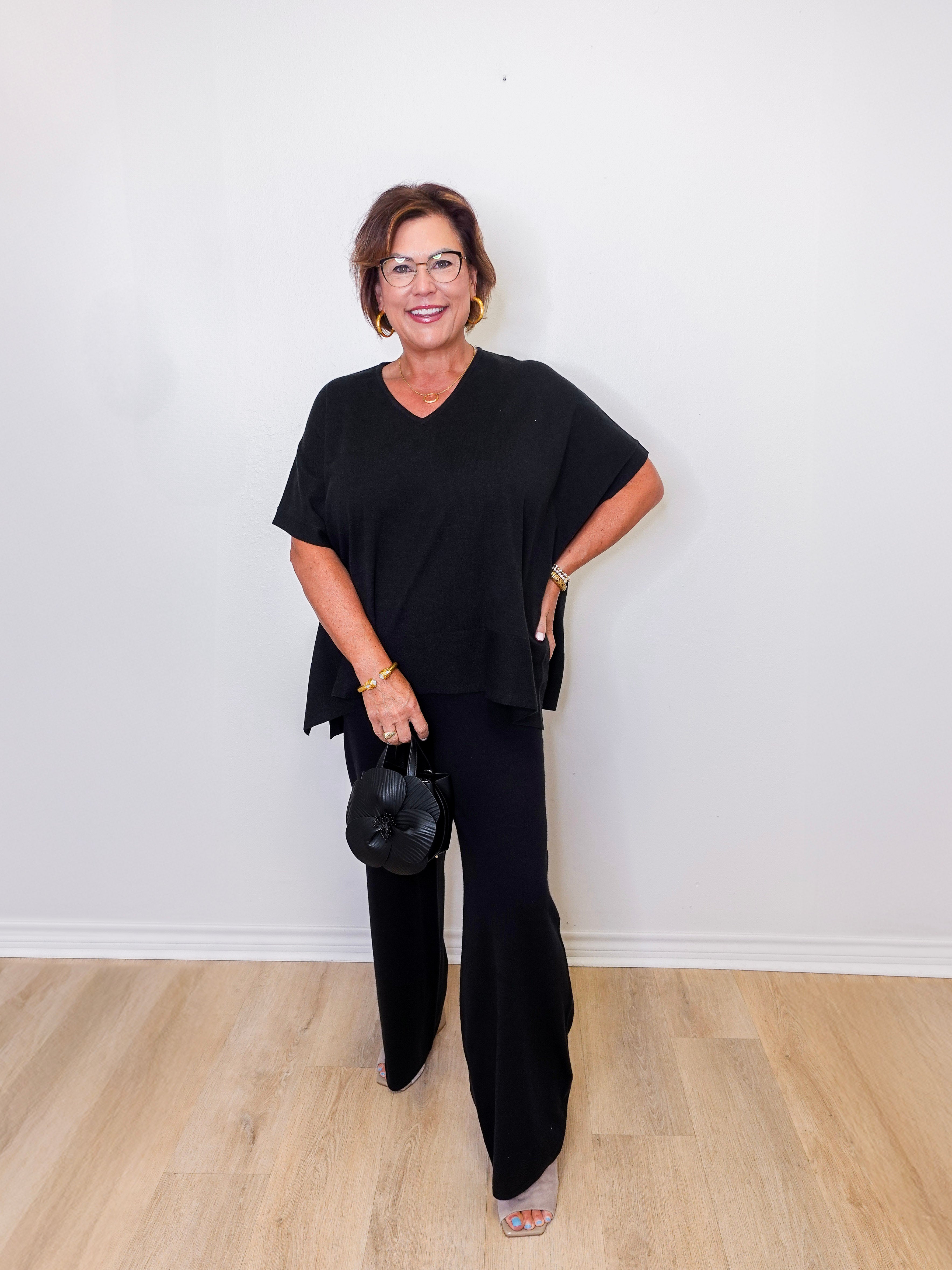 Woman wearing a black outfit standing against a white wall.