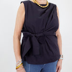 Woman wearing a navy sleeveless top with a bow detail and blue jeans on a white background