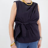 Woman wearing a navy sleeveless top with a bow detail and blue jeans on a white background