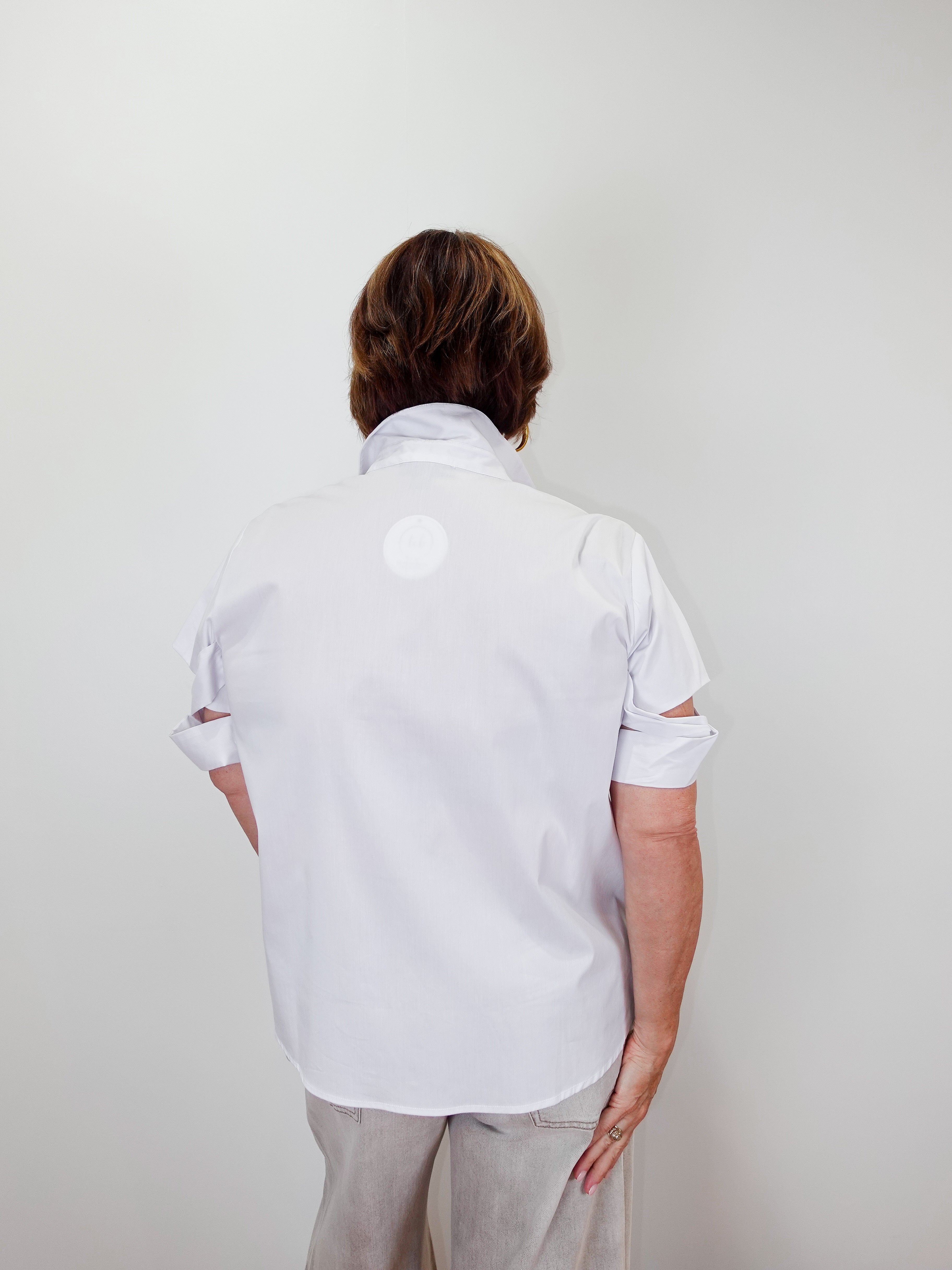 Person wearing a white shirt with cut-out sleeves against a plain background