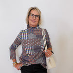 Woman wearing a patterned shirt and holding a white handbag against a plain background