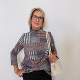 Woman wearing a patterned shirt and holding a white handbag against a plain background