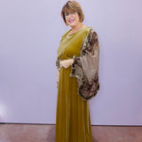 Woman wearing a green dress and patterned shawl against a plain background
