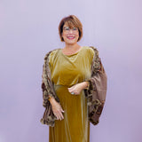 Woman wearing a green velvet dress with a brown shawl against a light purple background