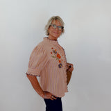Woman wearing a patterned blouse with floral designs against a plain white wall.