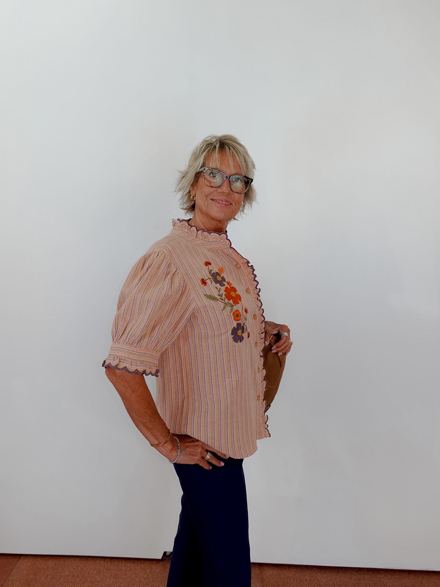 Woman wearing a patterned blouse with floral designs against a plain white wall.