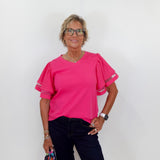 Woman wearing a pink blouse and dark pants against a white background