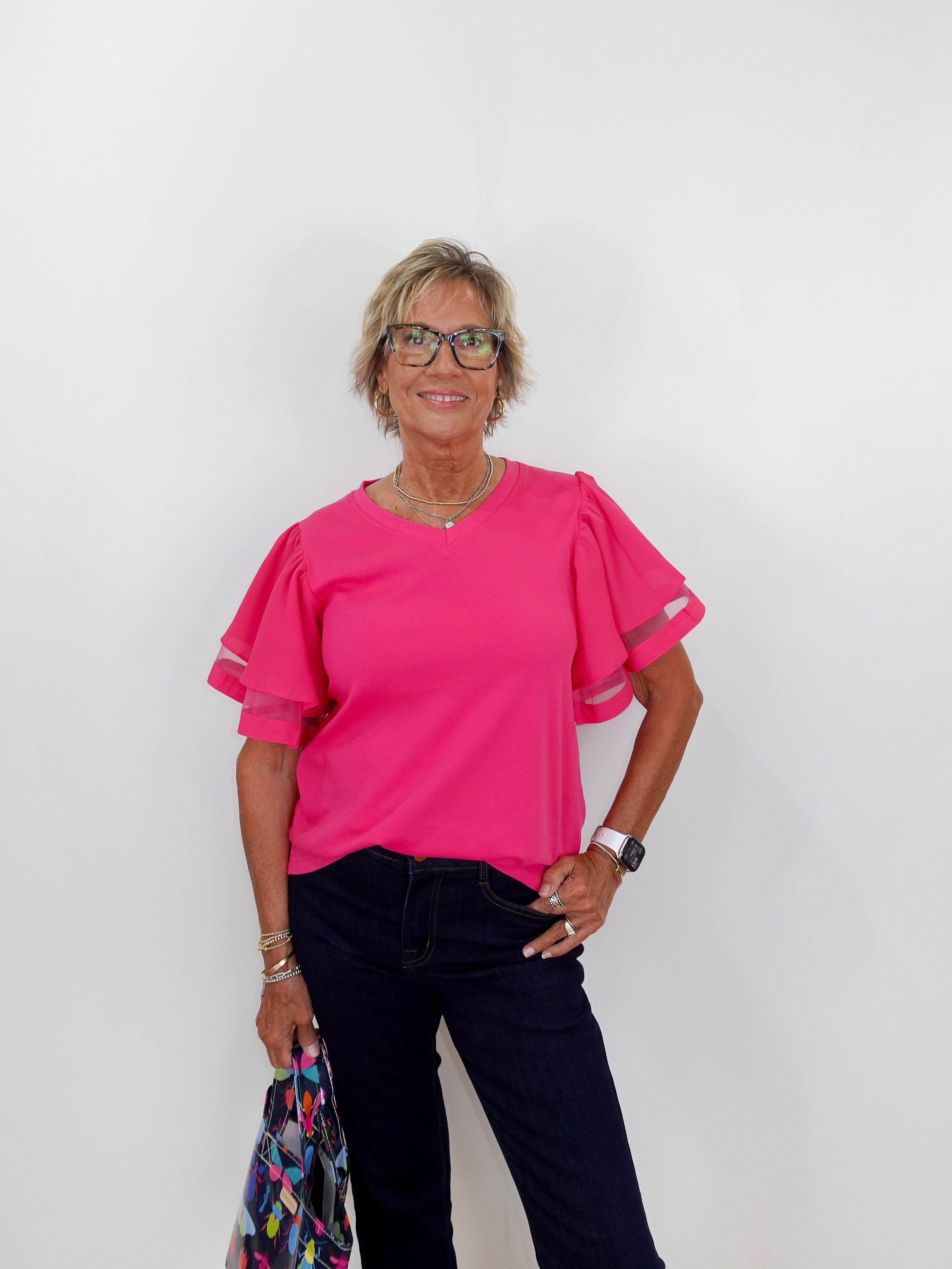 Woman wearing a pink blouse and dark pants against a white background