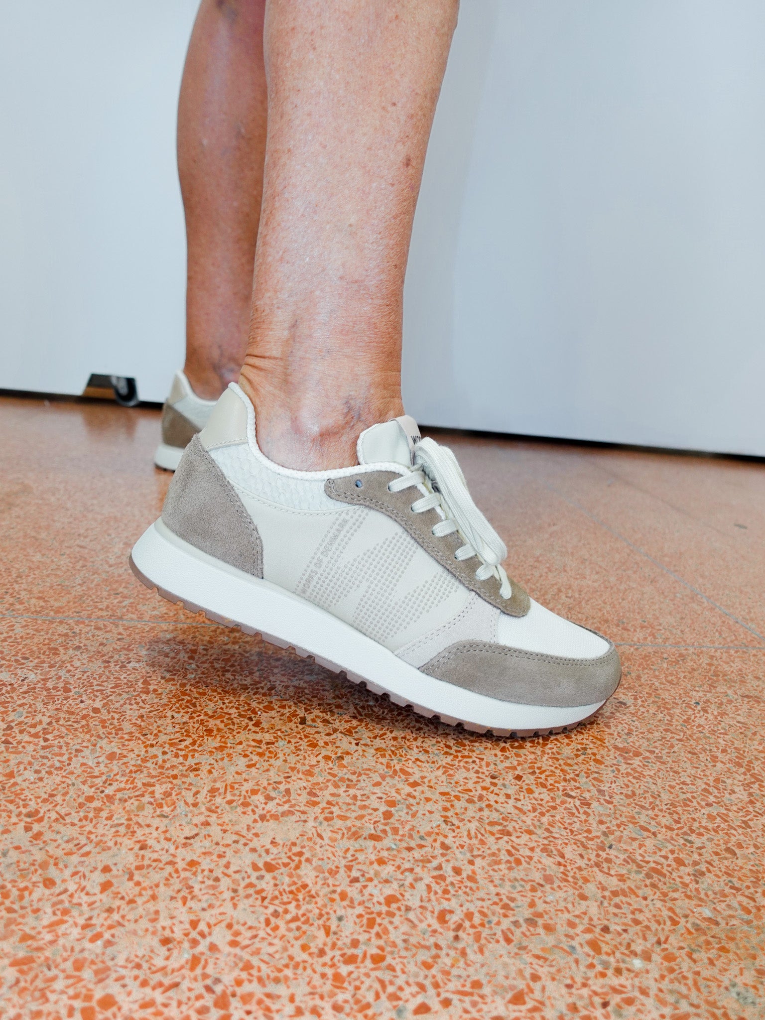 Person wearing gray and white sneakers on a speckled orange and brown floor.