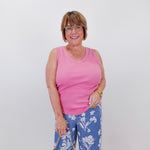 Woman wearing a pink tank top and blue floral pants, holding a beige handbag against a white wall.