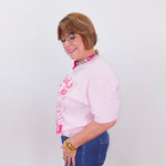 Woman wearing a pink blouse with a pattern and blue jeans against a white background