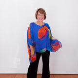 Woman wearing a colorful blouse and black pants against a white background