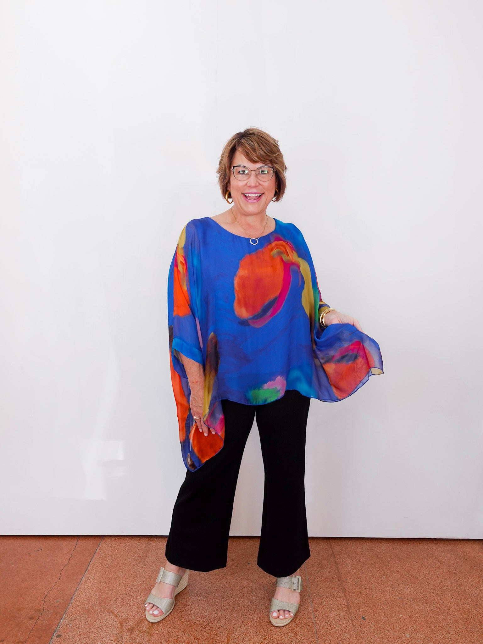 Woman wearing a colorful blouse and black pants against a white background