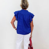 Person wearing a blue blouse and white pants, holding a red bag against a white background