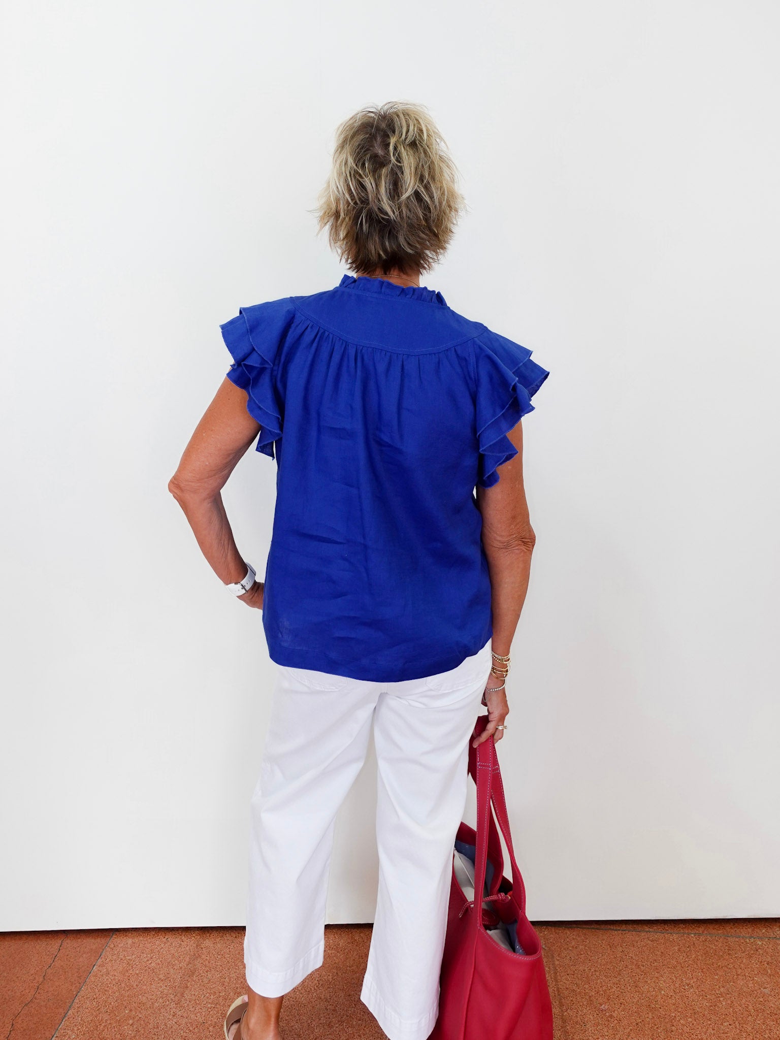 Person wearing a blue blouse and white pants, holding a red bag against a white background